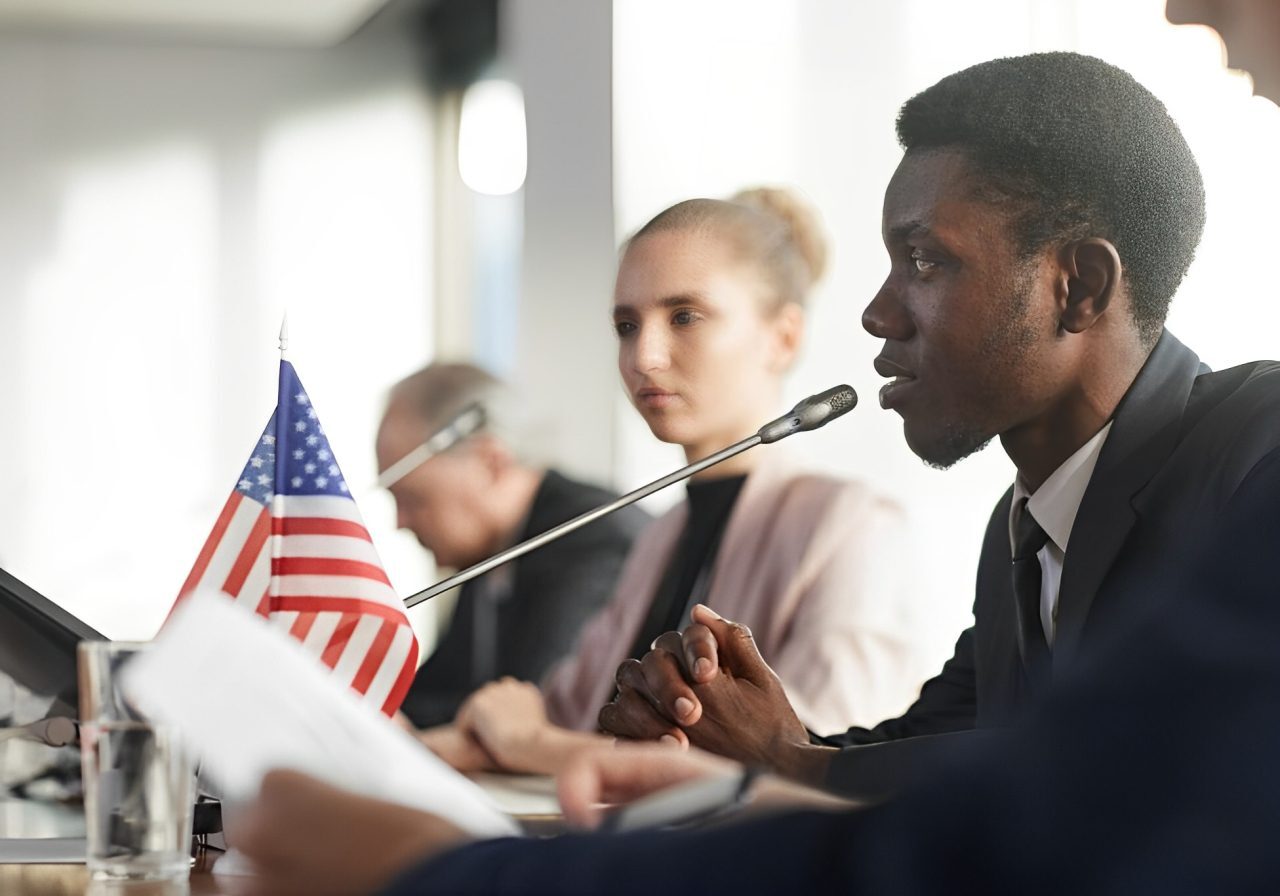A man is speaking at a meeting with other people.